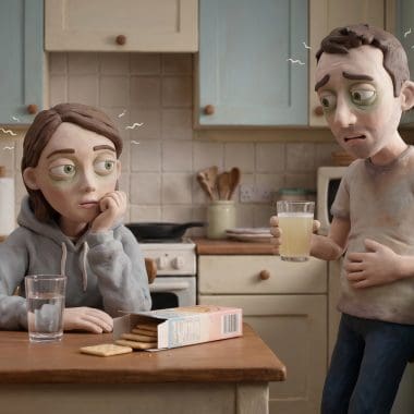 Image of hangover nausea — a man and woman in Aardman claymation style looking queasy together in a morning kitchen, crackers and electrolyte drink on the counter.